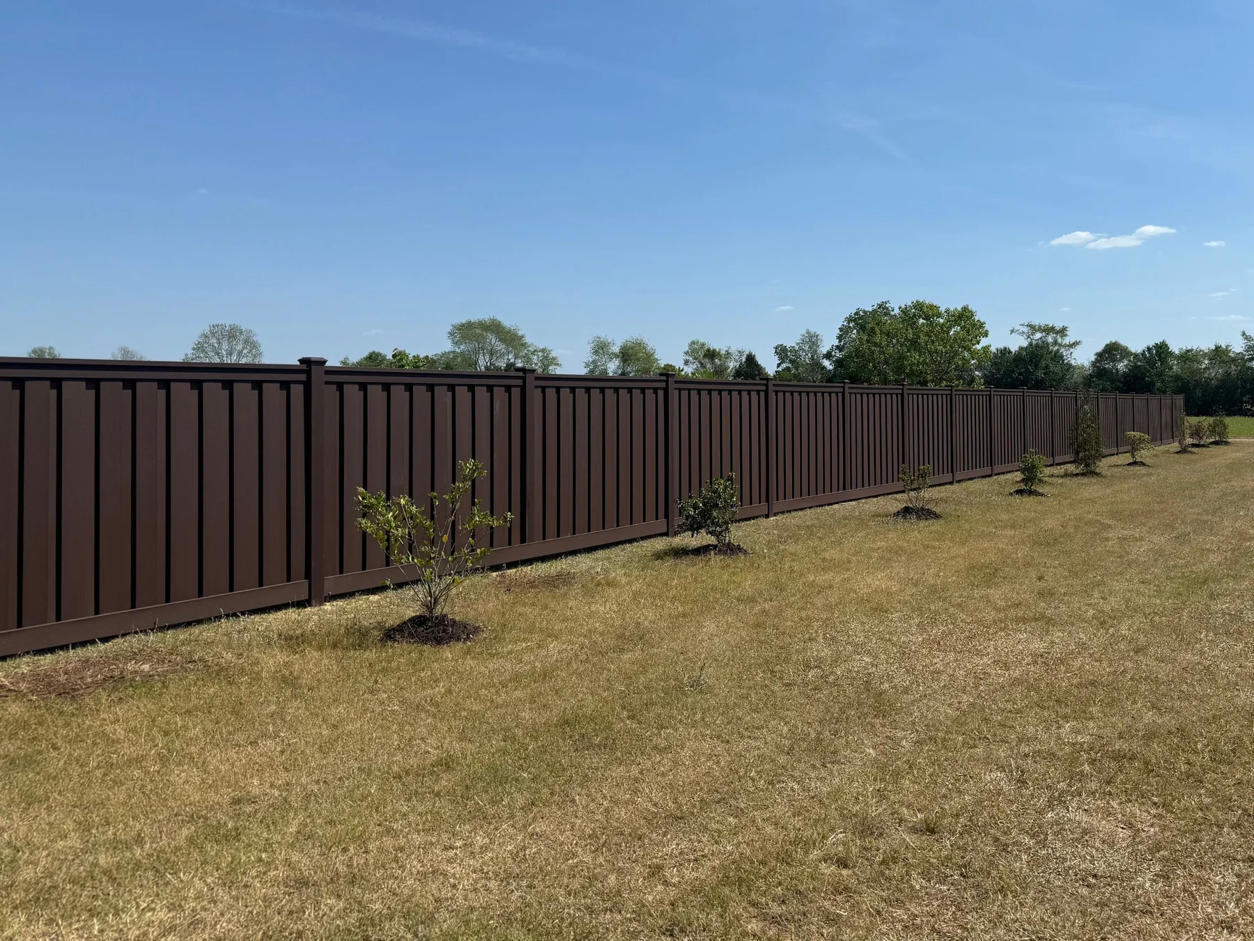 Long brown composite privacy fence installed across a landscaped property